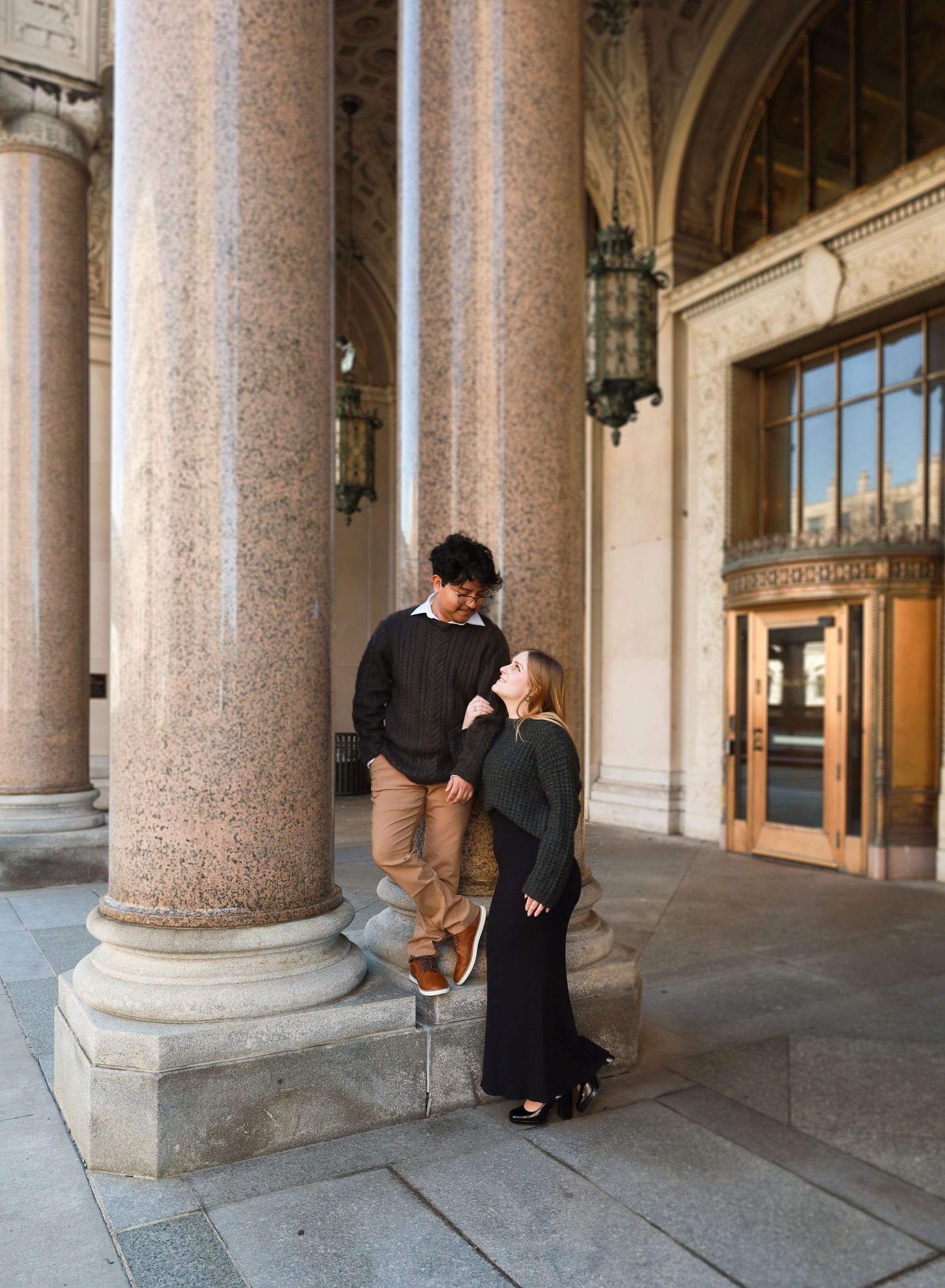 A couple shares an intimate moment between grand columns in a historic building.