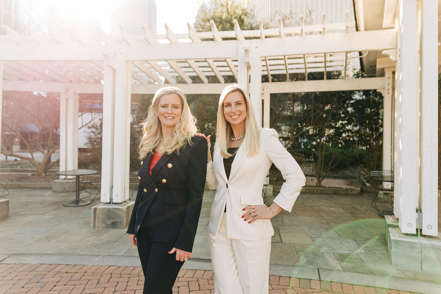 Two women stand together under a white pergola, one wearing black and one in white professional attire in Uptown Charlotte for Forbes
