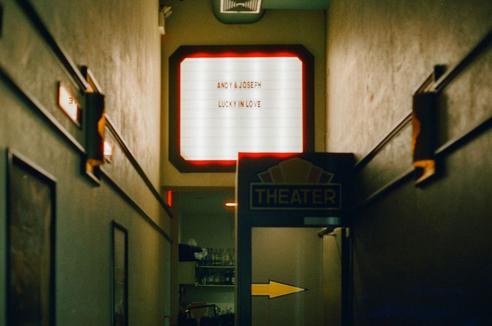 A dimly lit theater corridor with a glowing marquee sign and arrow pointing to the entrance.