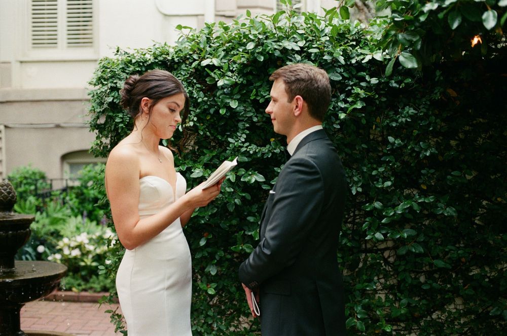 A couple shares a private moment during their wedding ceremony in a garden setting with lush greenery.