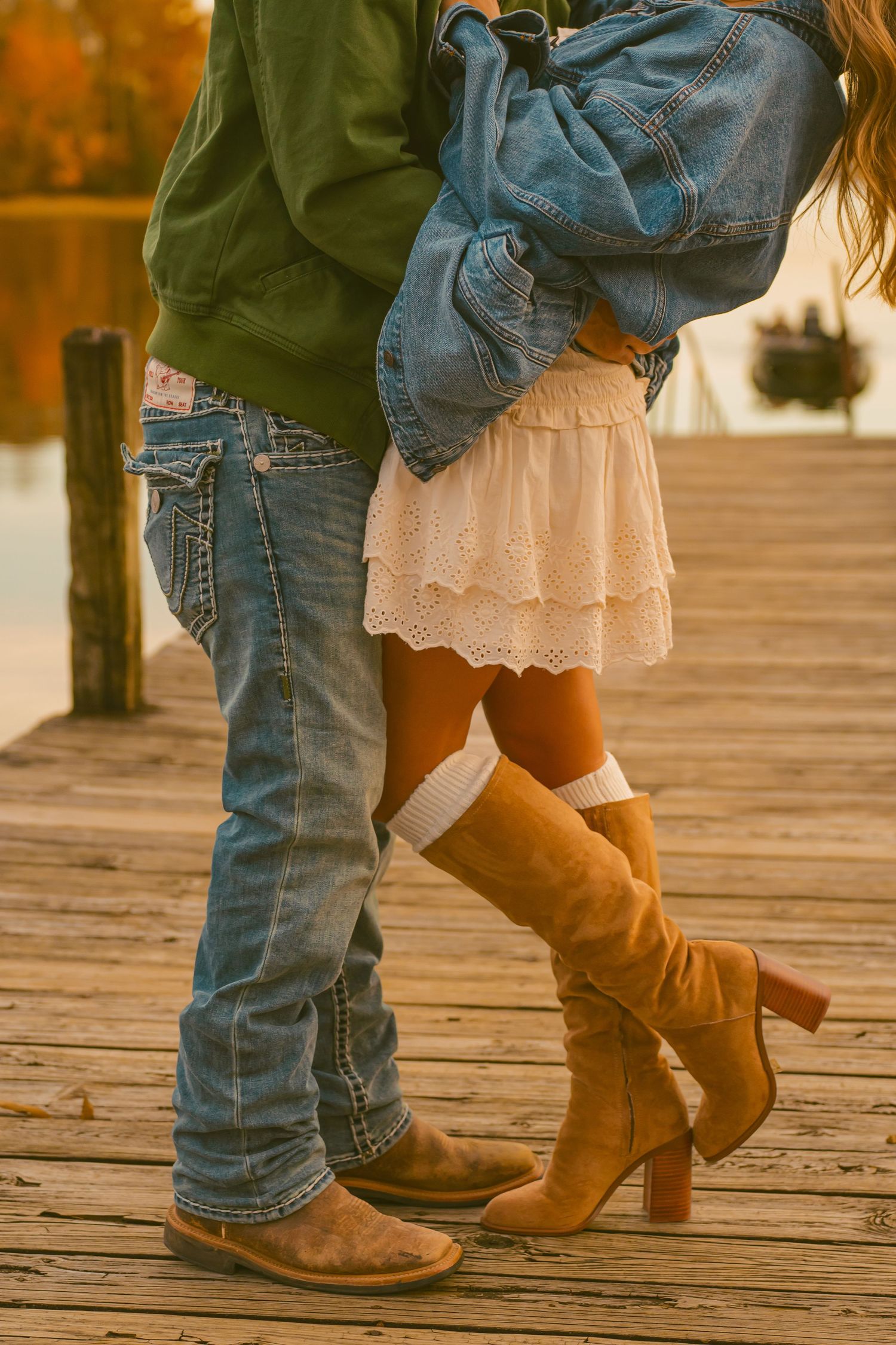 A romantic couple embracing on a wooden deck wearing denim, a lace skirt and brown boots in autumn lighting.