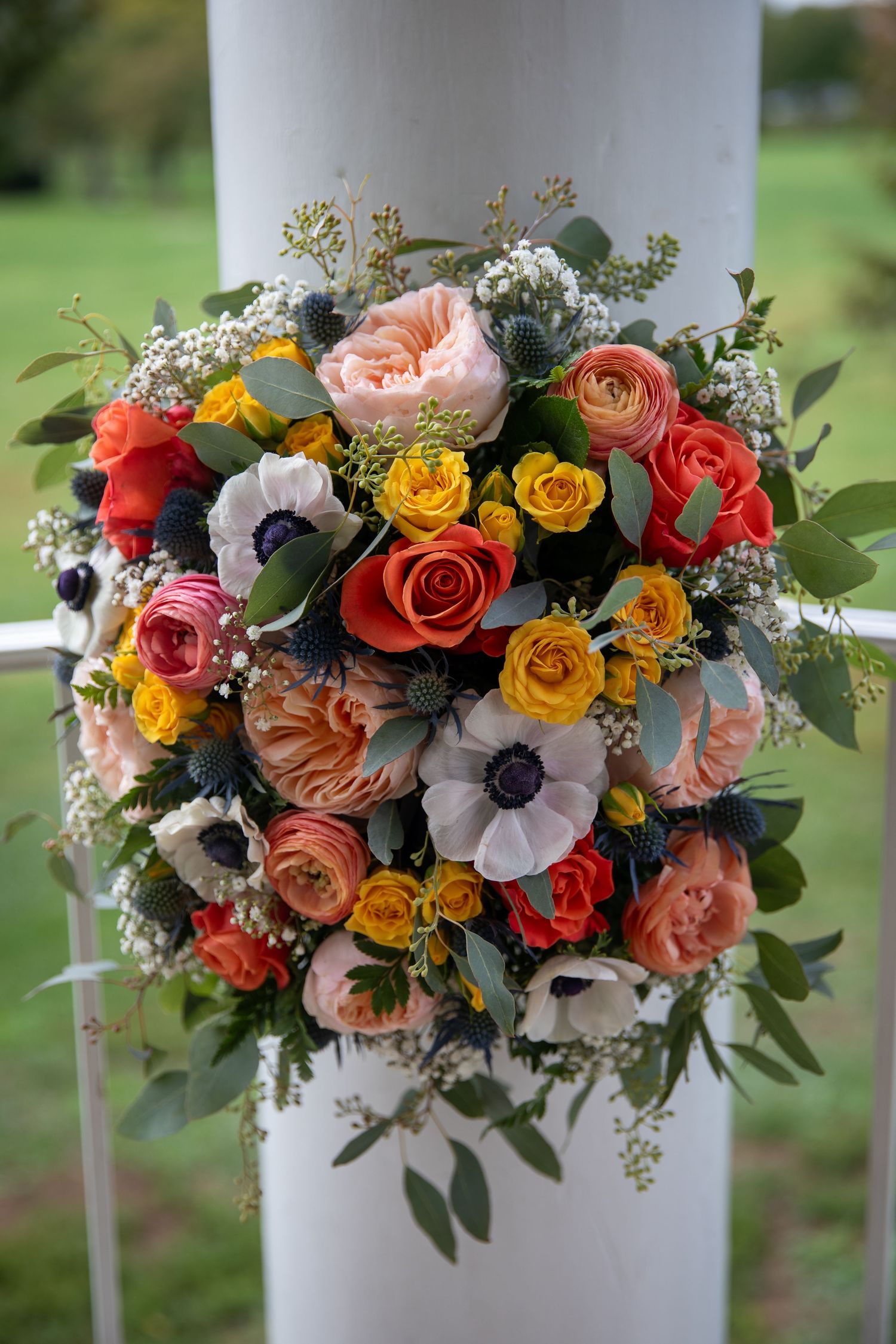 frederick county wedding photography Vibrant floral arrangement with coral, yellow and white flowers adorns a white column outdoors.