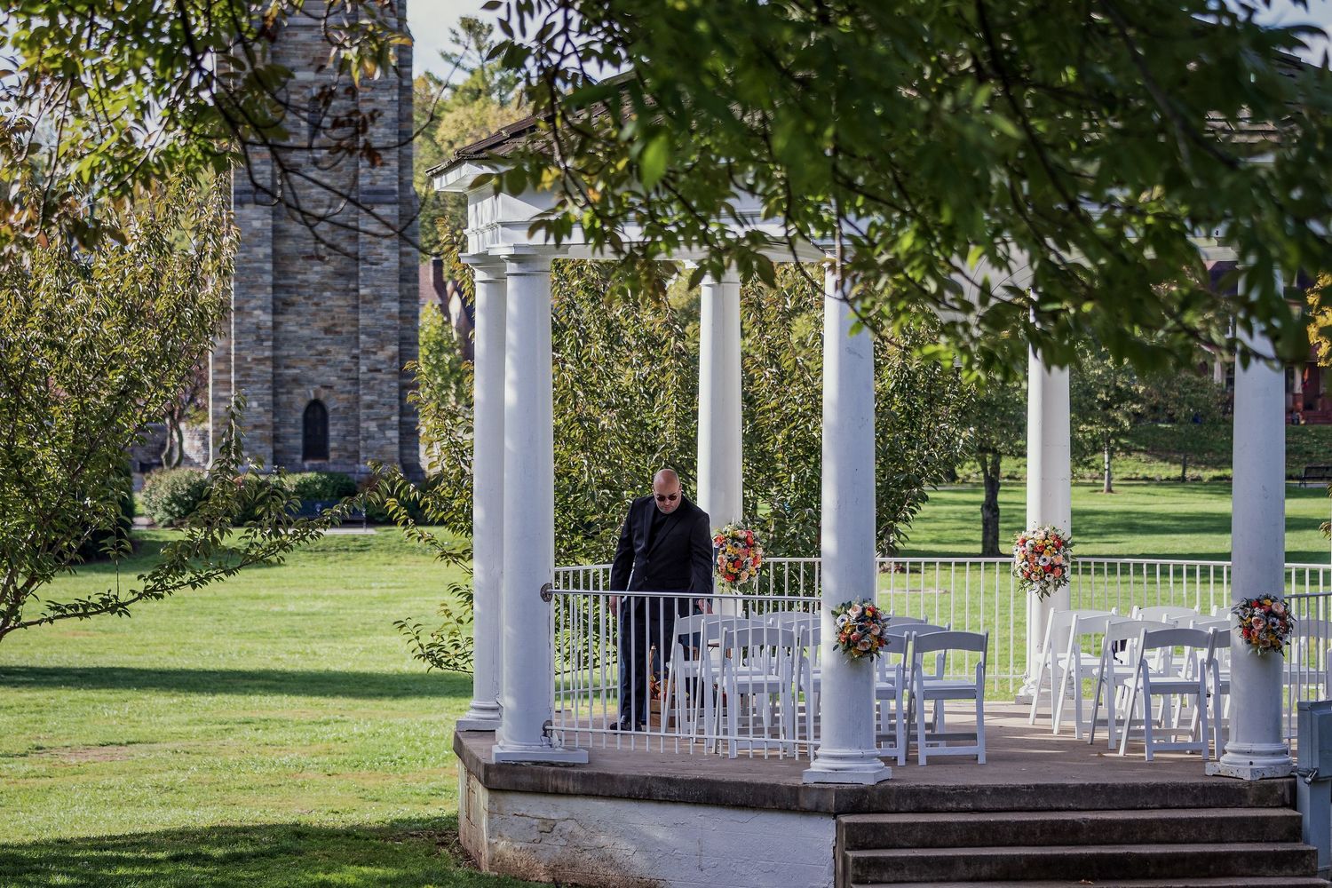 frederick county wedding photography White gazebo with columns stands in a scenic park setting with green grass and trees.