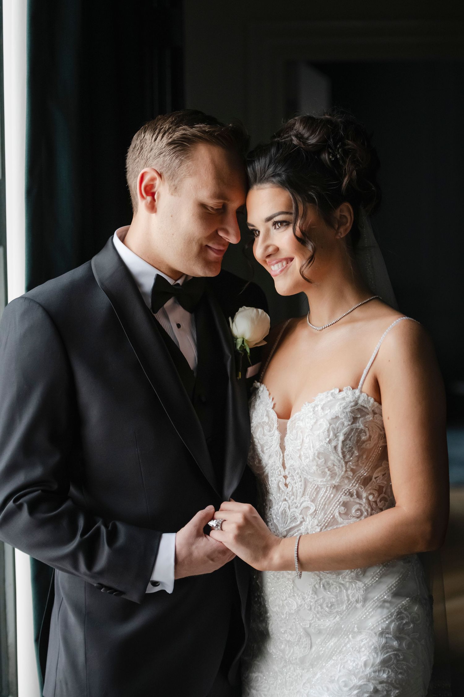 A romantic wedding couple shares an intimate moment by large windows, captured in the presidential suite of Philadelphia's Bellevue Hotel