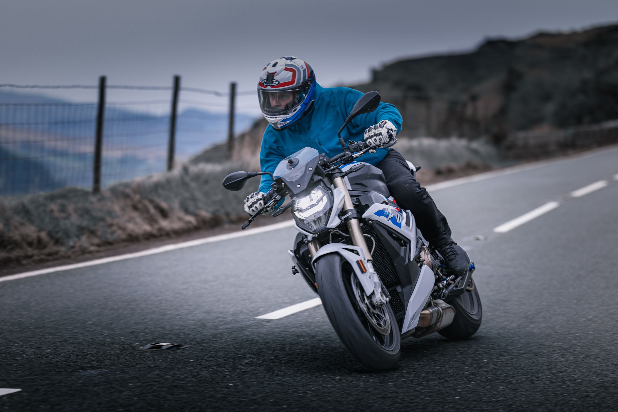 A motorcyclist leans into a curve on a coastal mountain road while riding a sport bike at sunset.