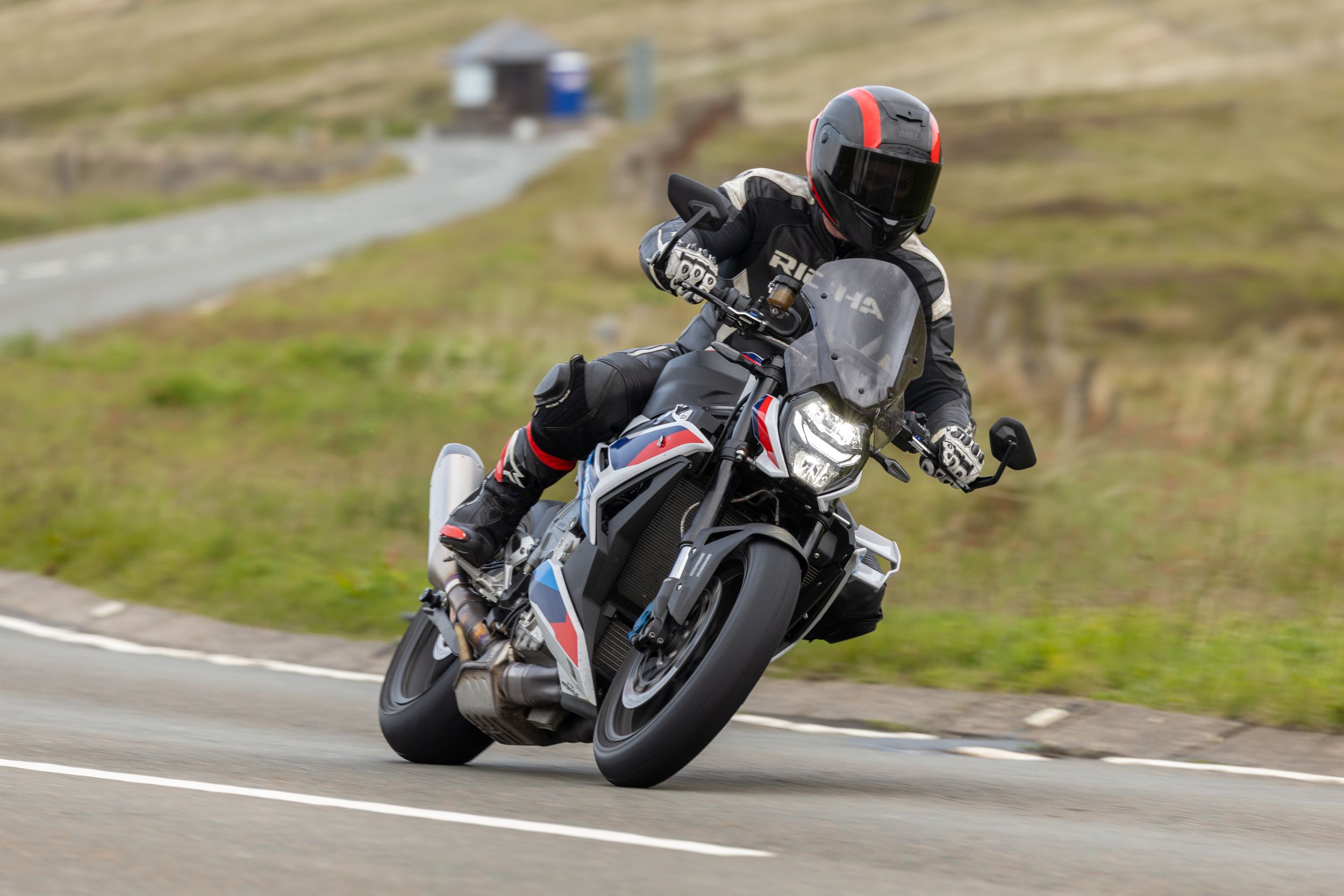 Motorcyclist riding a sport bike on a winding mountain road with a car visible in the background.