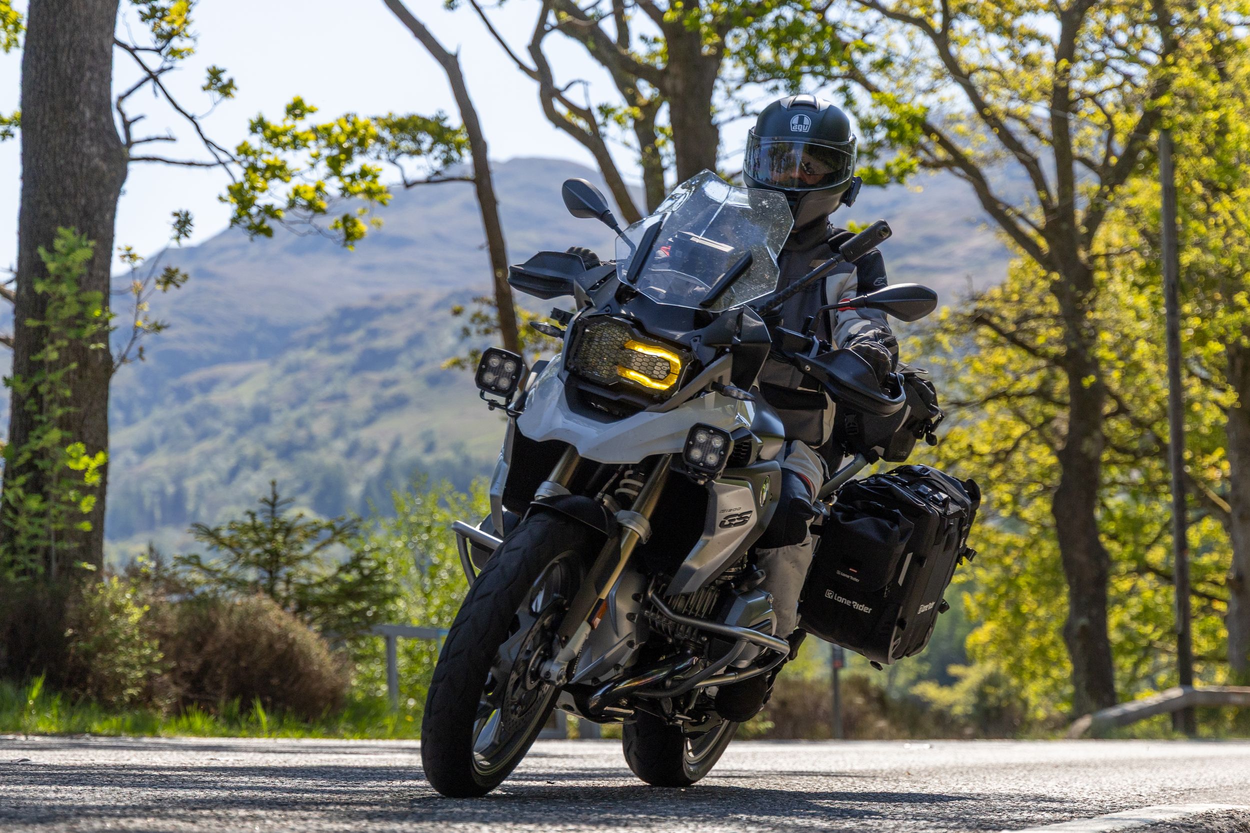 Adventure motorcycle rider navigates a winding mountain road through autumn trees with scenic valley views.