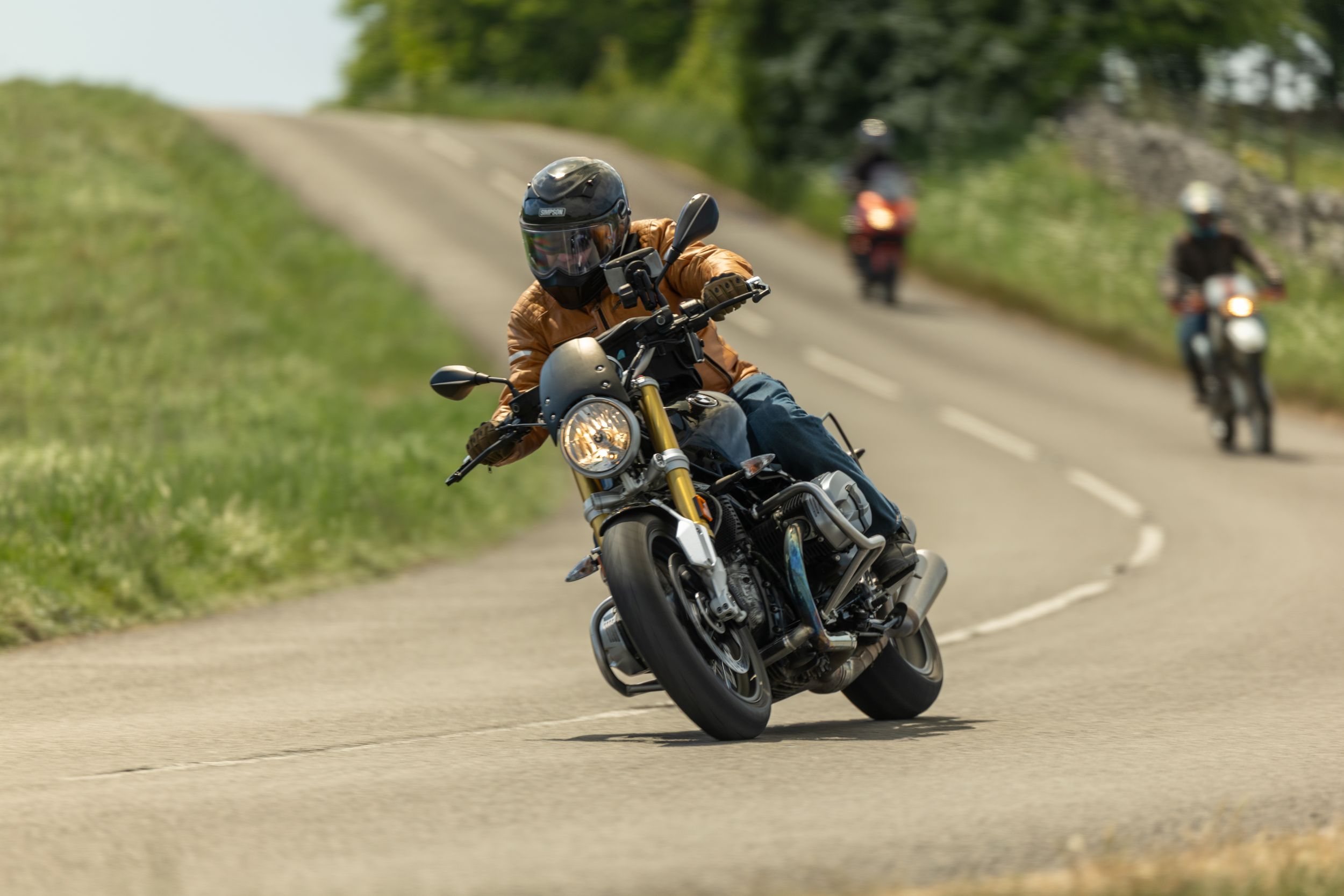 Motorcyclists ride in formation on a winding mountain road during a scenic group ride through green countryside.