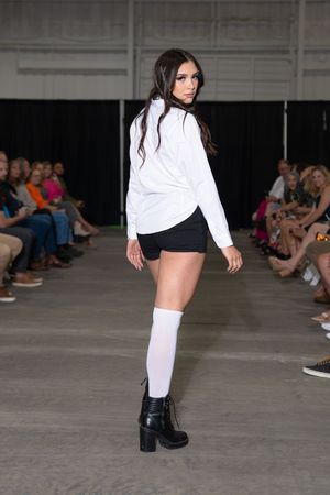 Model showcases white long-sleeve top with black shorts and platform boots on industrial runway.