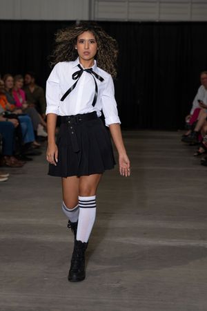 Models showcase a modern schoolgirl-inspired fashion collection featuring white blouses and black skirts on the runway.