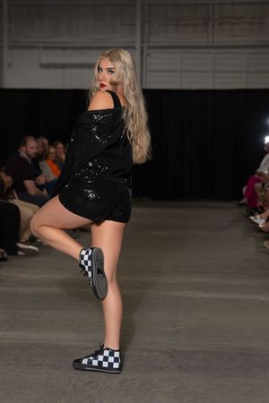 Dancer performs in black sequin outfit and checkered slip-on shoes on industrial stage.