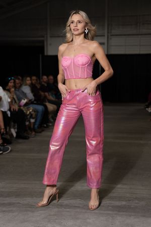 Model showcases pink leather pants and matching bustier on industrial-style fashion runway.