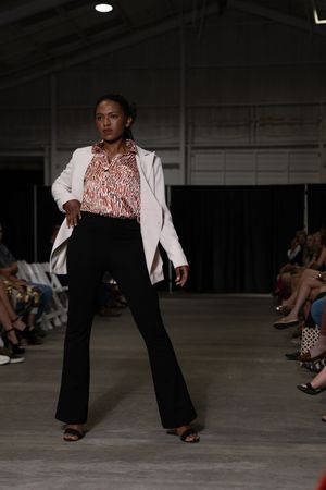 Fashion model walks runway in white blazer and black pants during warehouse fashion show.