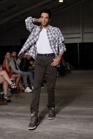 Model performs breakdance moves on runway wearing plaid shirt and dark pants.