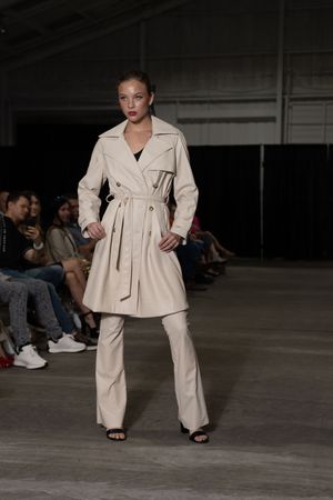 Model showcases cream-colored belted pantsuit ensemble on industrial-style runway.
