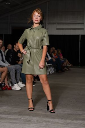 Model showcases an olive green military-inspired dress with black heels on the catwalk.