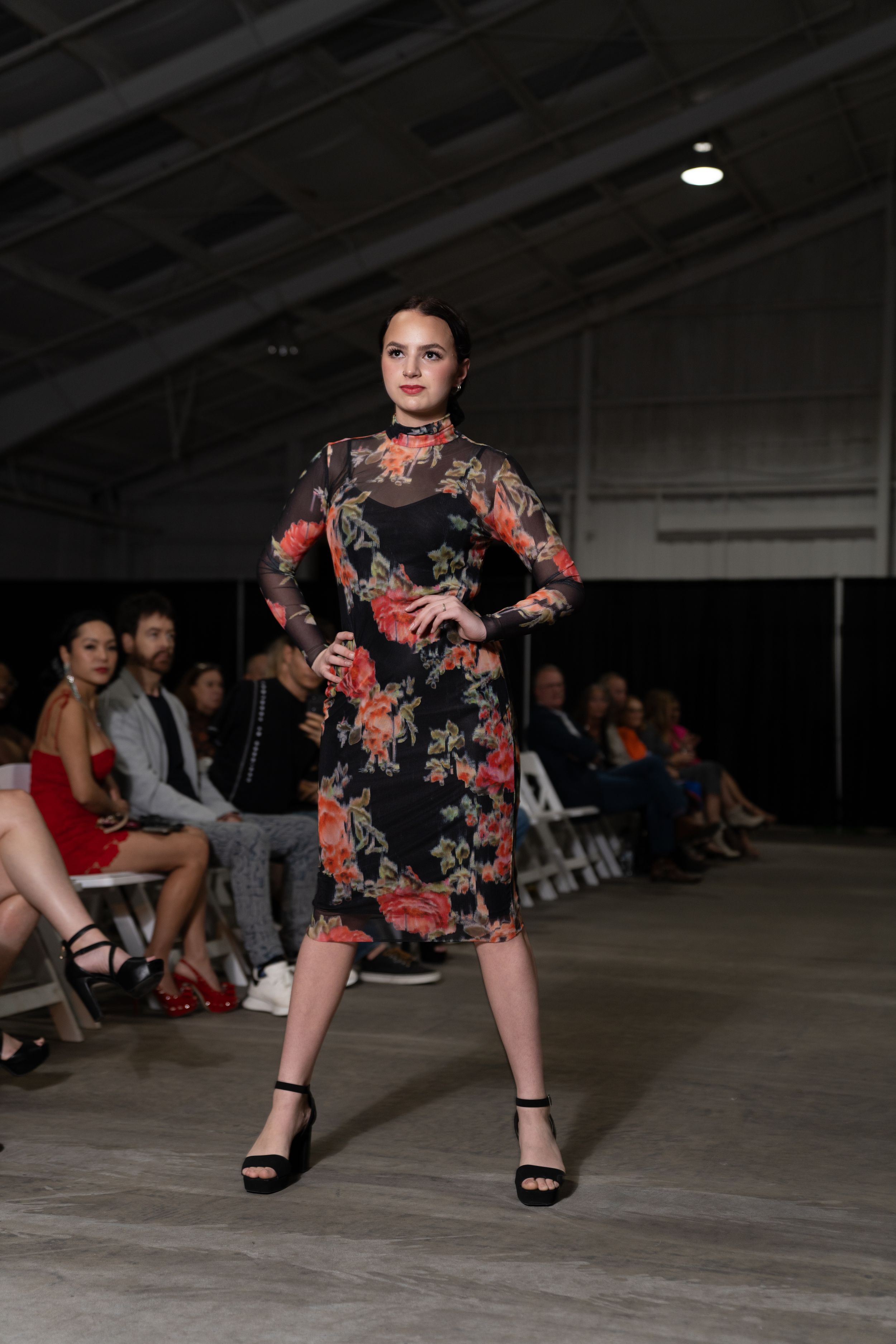 Model in floral print dress strikes dynamic pose while walking runway at indoor fashion show.