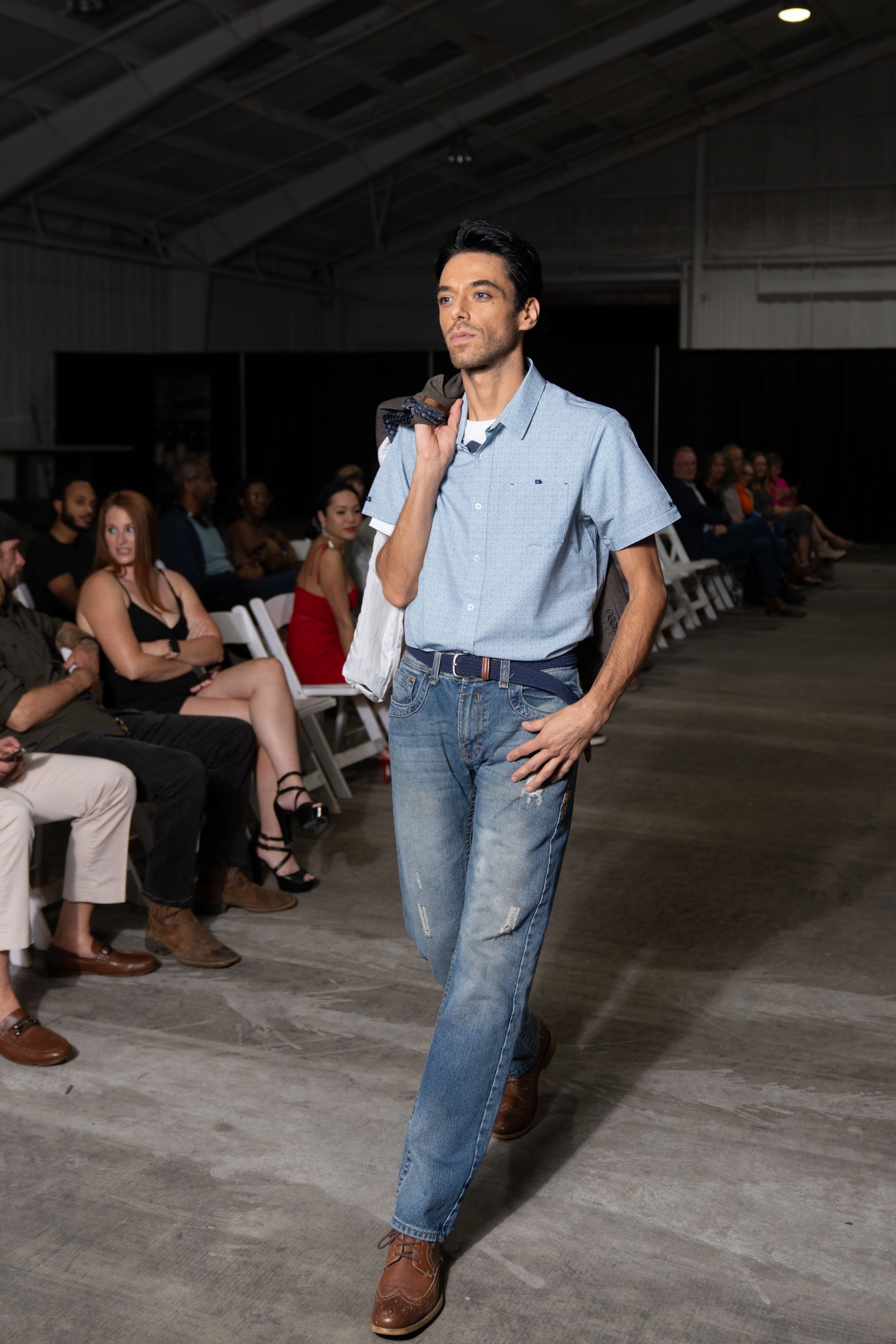 Model walks runway in light blue button-down shirt and relaxed-fit jeans during casual fashion show.