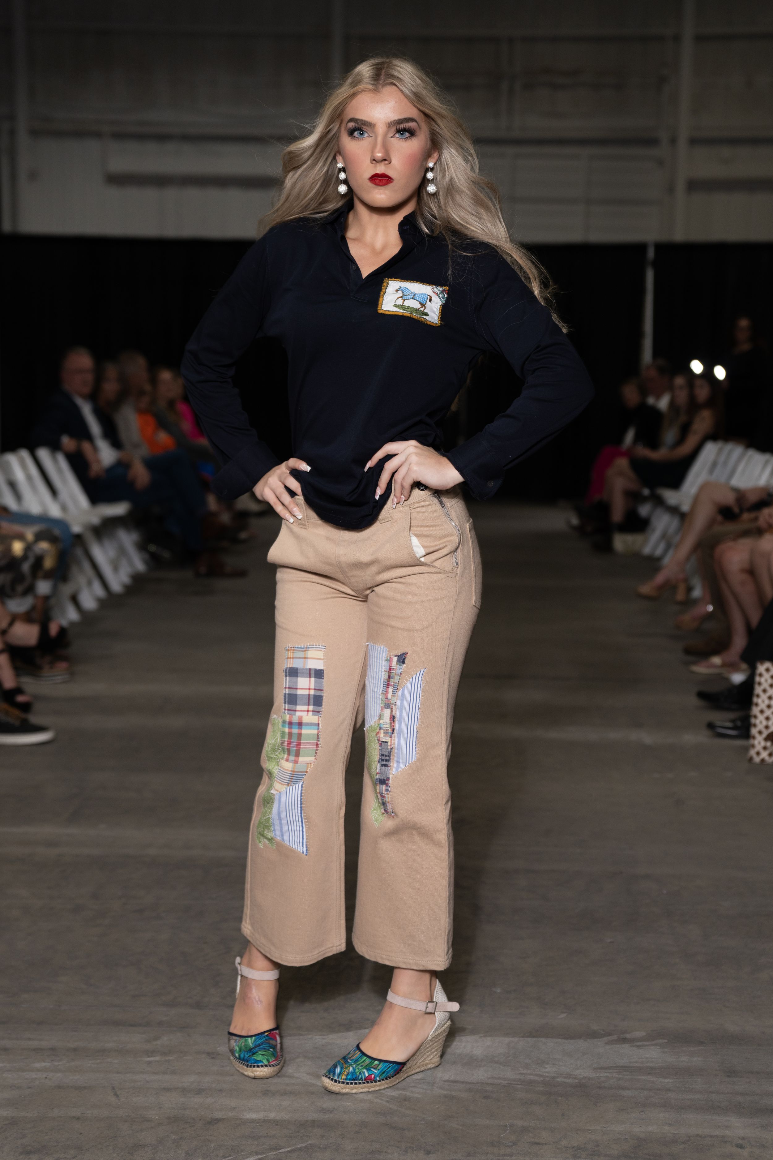 Fashion model wearing navy sweater and khaki pants with patchwork details on catwalk.