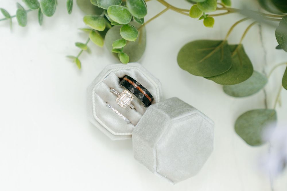 Wedding rings displayed in a gray velvet octagonal ring box surrounded by eucalyptus greenery.