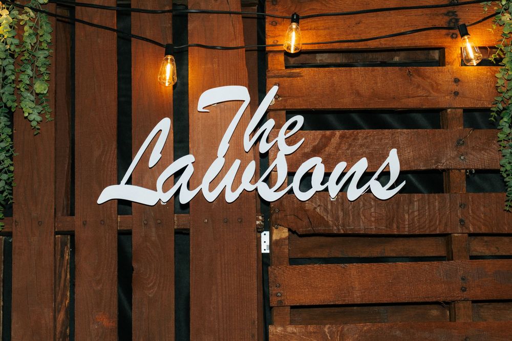 Rustic wooden sign reading The Lawsons decorated with string lights and ivy for a wedding.