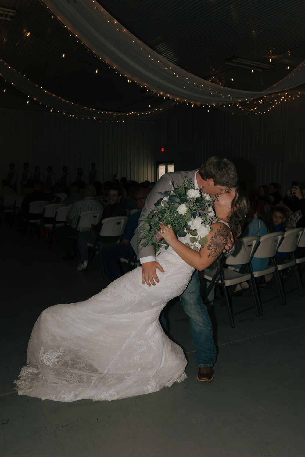 Groom dipping bride for a romantic kiss while holding bouquet during wedding ceremony.