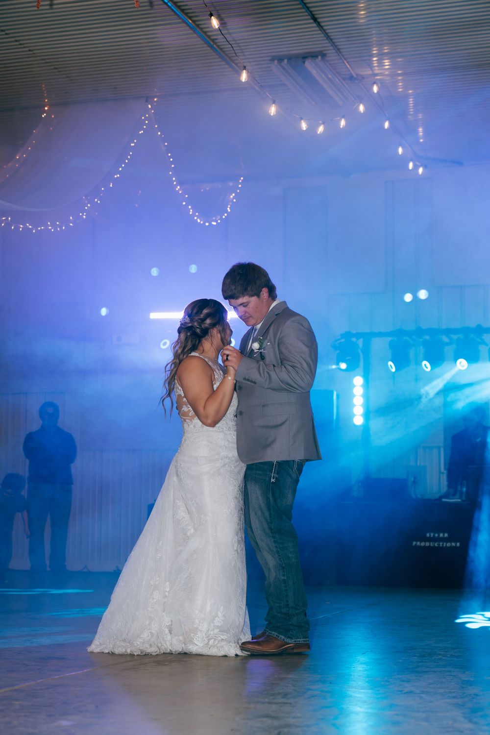 Bride and groom sharing their first dance under blue lights and string lights at reception.