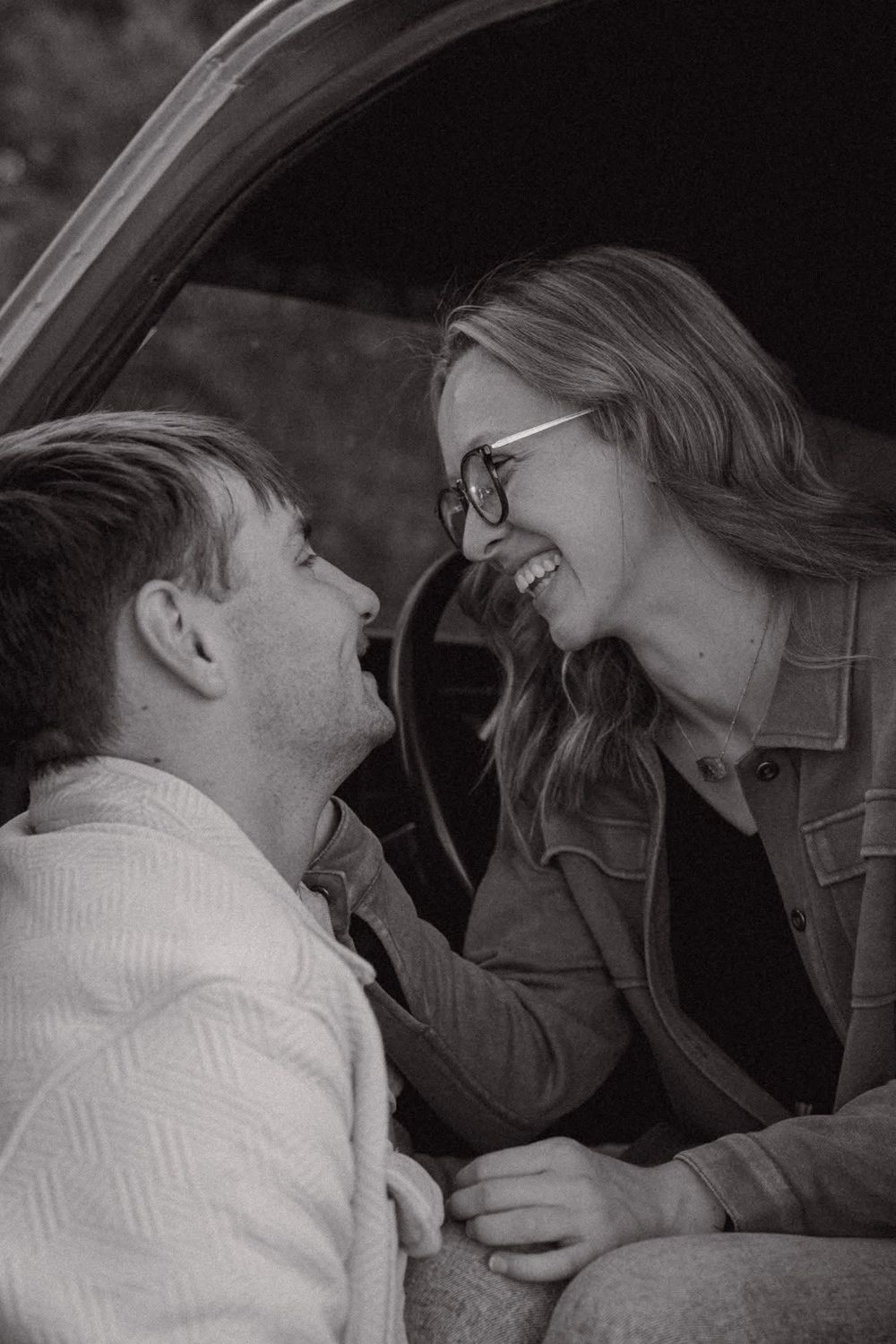 Black and white photo of a laughing couple sitting together in the trunk of a car.