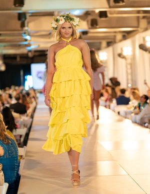 Model walks runway in bright yellow ruffled halter dress during fashion show presentation.