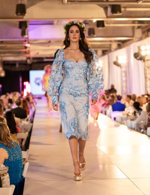 Models showcase light blue lace dresses on an illuminated runway with purple accent lighting.