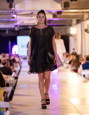 Fashion models present black sheer outfits on an illuminated catwalk with purple lighting accents.