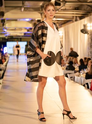 Fashion models showcase black and white ensembles on a brightly lit catwalk with audience in background.