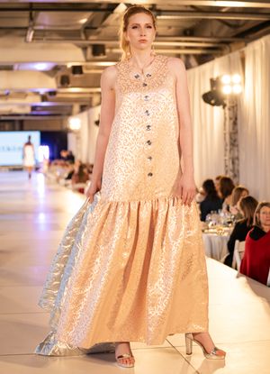 Models showcase elegant champagne-colored floral dresses on illuminated catwalk.