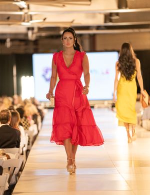 Models in vibrant red and yellow dresses glide down bright white runway during fashion show.