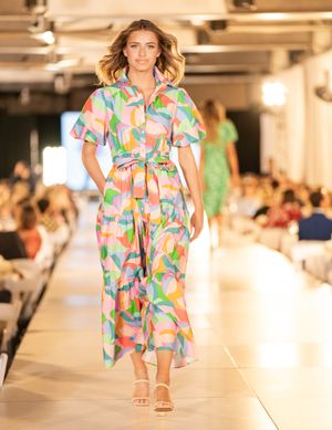 Models present colorful tropical print dresses on white catwalk during indoor fashion event.