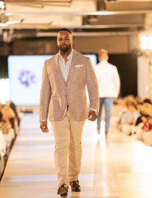 Men model checkered blazers and cream pants on a softly lit fashion runway.