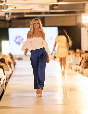 Fashion show models walking down illuminated catwalk wearing navy blue resort wear designs.