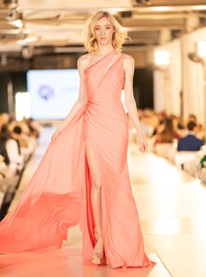 Model walks runway in flowing peach-colored gown during fashion show with elegant movement.