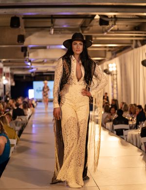 Fashion models present lace and fringe designs on a brightly lit catwalk.