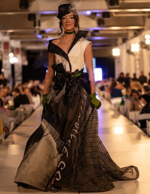 Models showcase elegant black evening gowns on an illuminated runway during a fashion show.