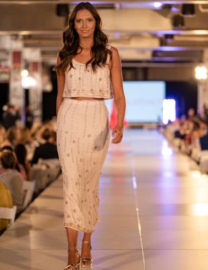 Fashion model walks runway in sleeveless white embellished summer dress at fashion show.
