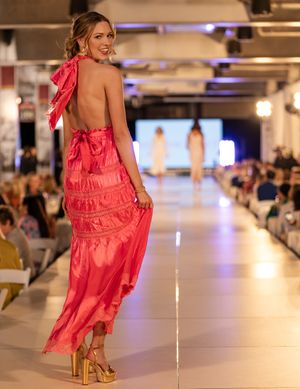 Model showcases ruffled coral dress with backless design on illuminated catwalk.