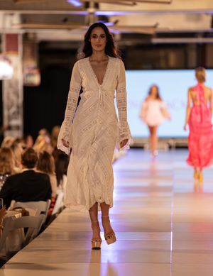 Models showcase flowing white lace dresses on illuminated runway during fashion event.