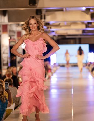 Models present pink ruffled cocktail dresses on brightly lit catwalk.