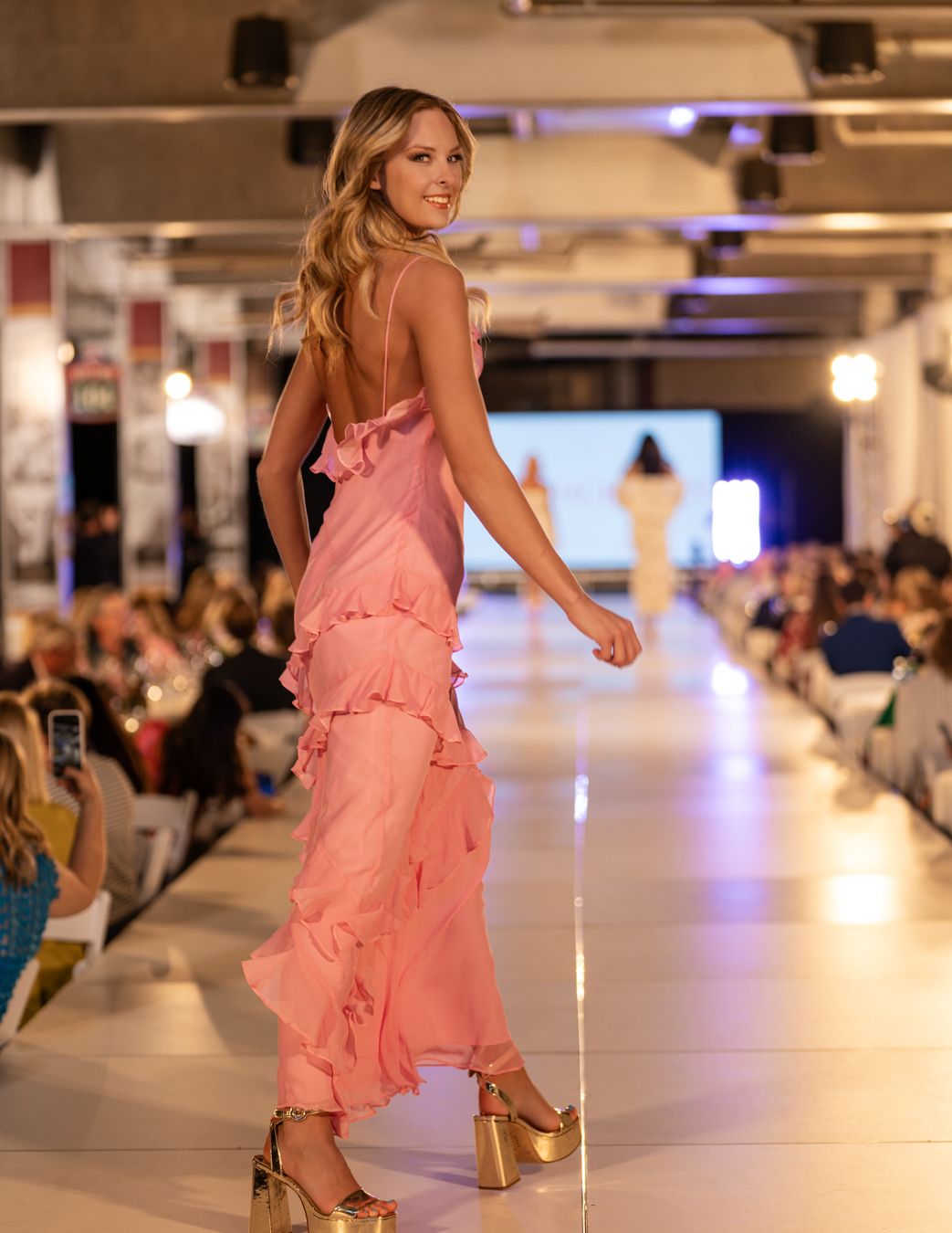 Models display ruffled pink dresses while strutting down an illuminated catwalk.