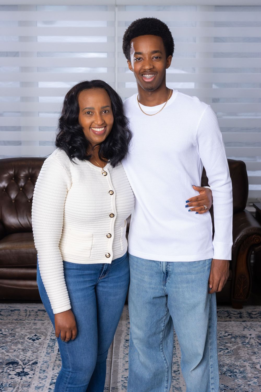 A couple wearing matching white tops and blue jeans pose together in a living room setting.