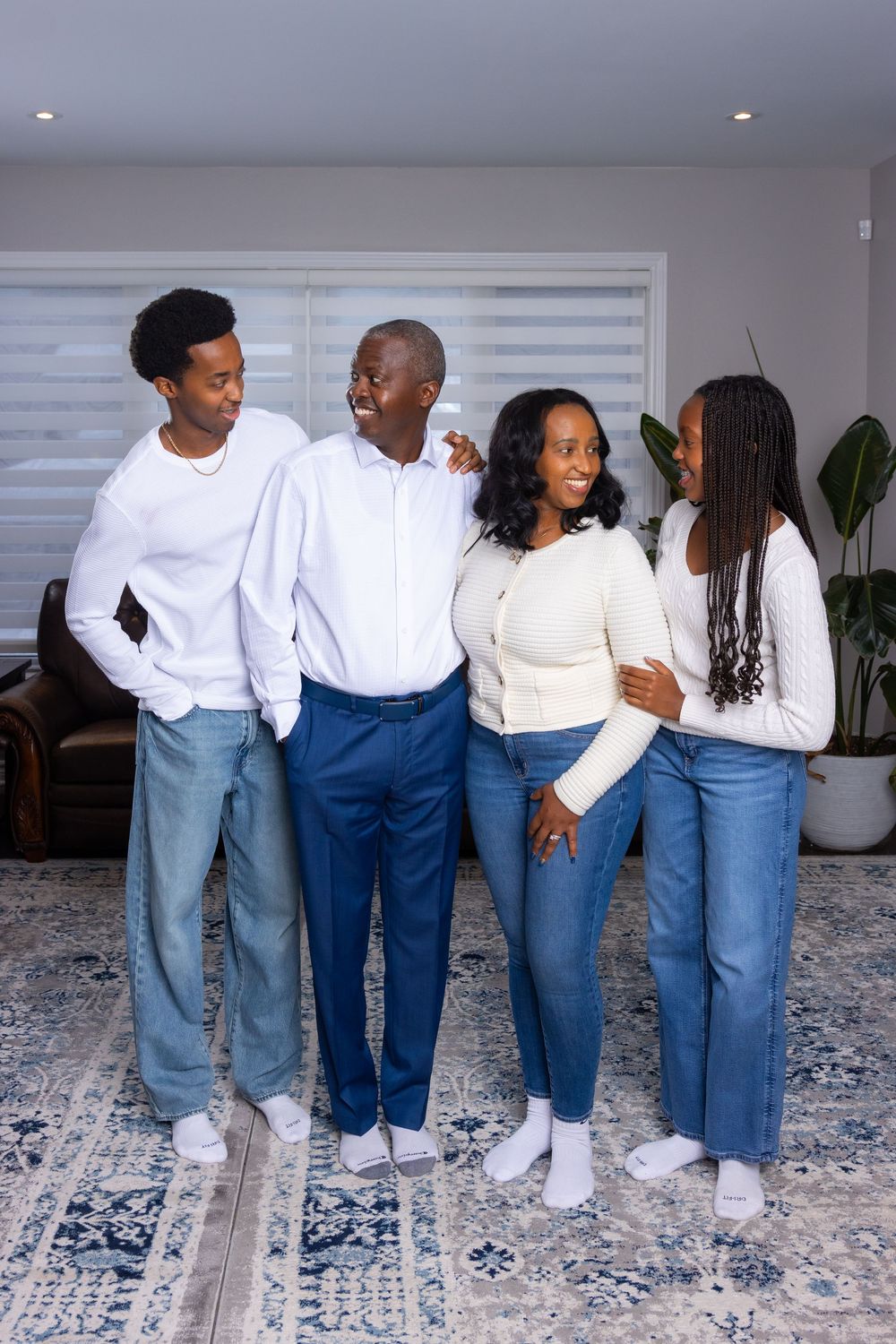 Family wearing coordinated outfits of white tops and blue jeans pose together on a patterned area rug.