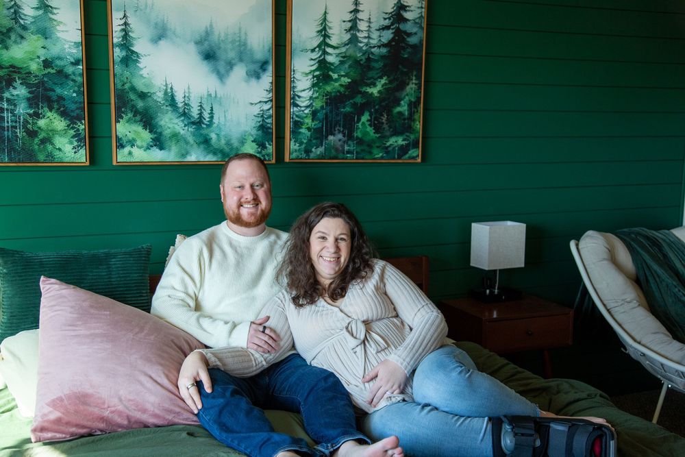 Husband and pregnant wife smiling together on their bed.
