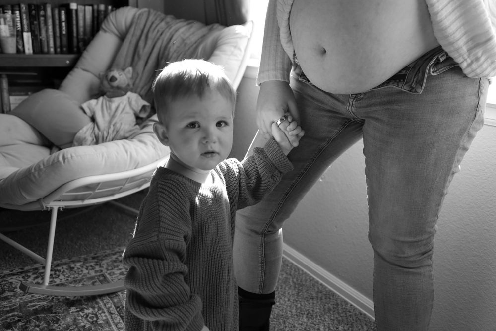 Young son holding hand of his mother by the window in bedroom.