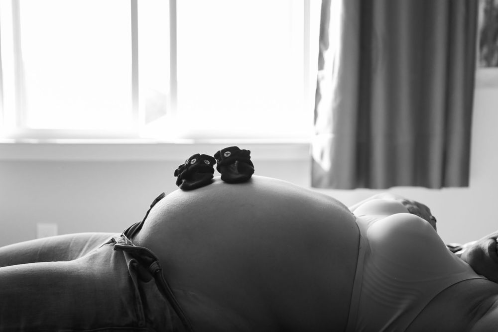 Pregnant woman laying on bed in front of a window.